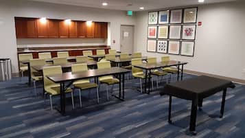 Un salón de conferencias con mesas y sillas, una kitchenette y cuadros en la pared.