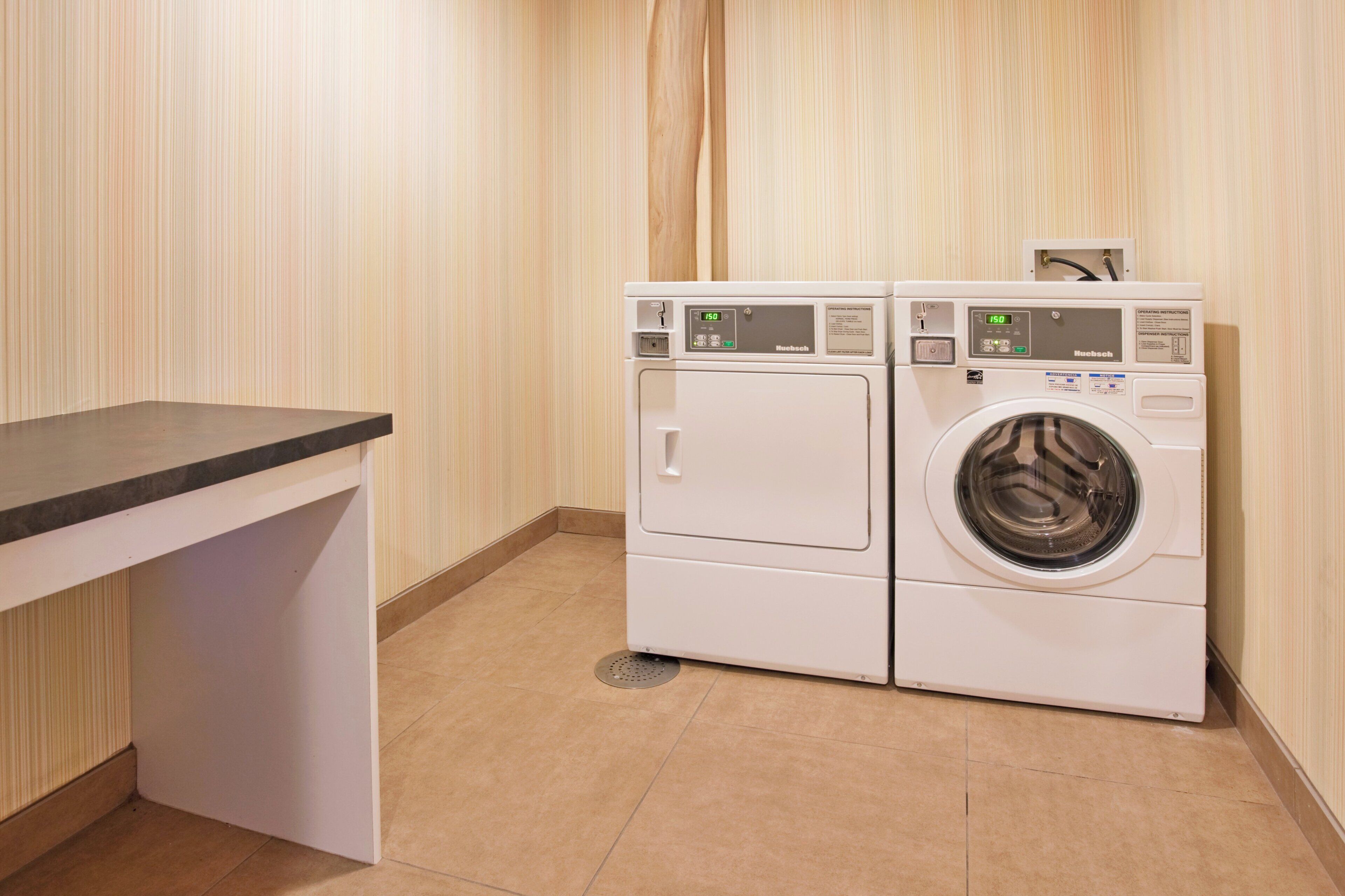 A laundry room with two stacked front-loading washing machines, a control panel, and a small table.