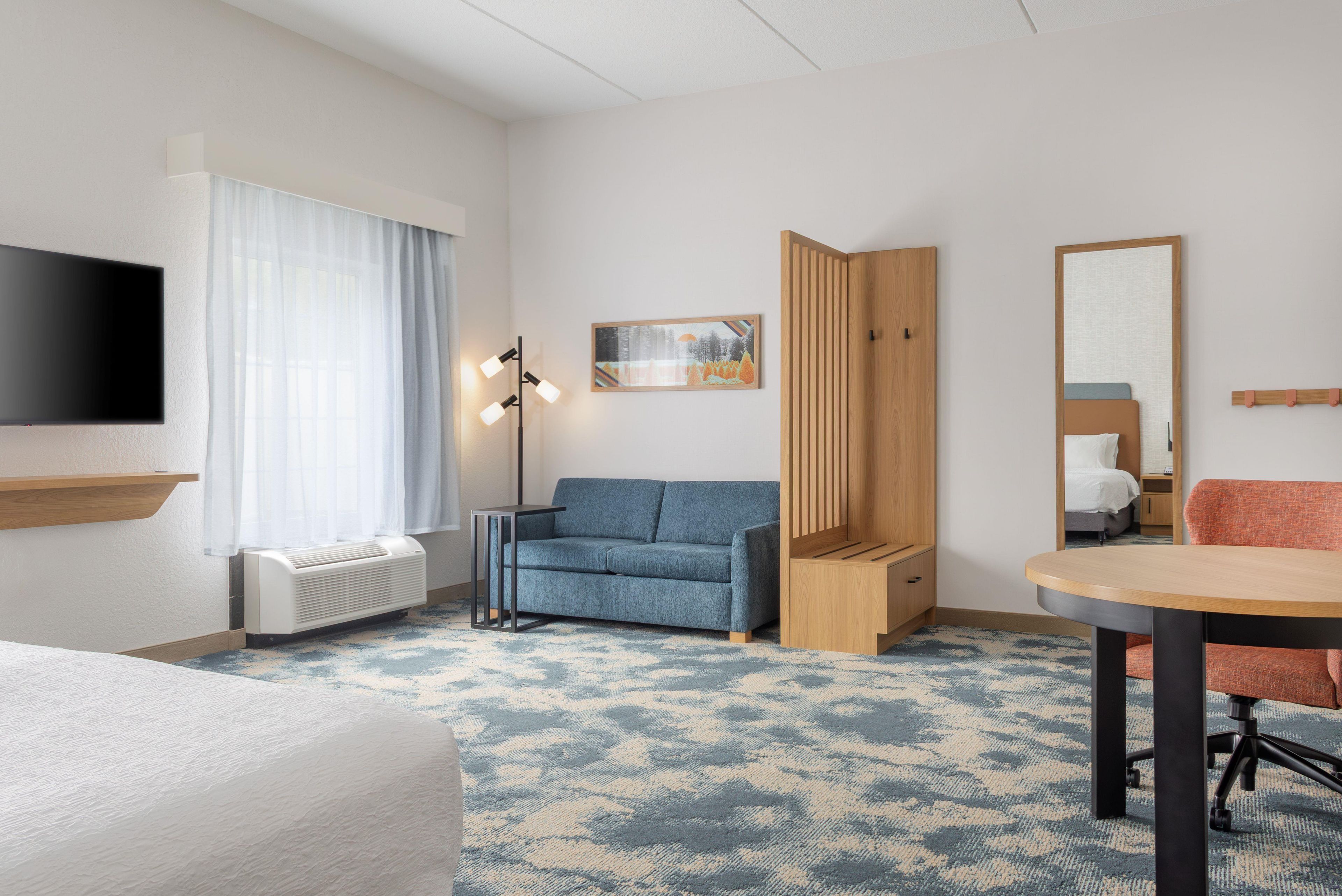 Une chambre d’hôtel comprenant un lit, un canapé, un bureau, une télévision, une fenêtre avec des rideaux, un tableau et un miroir.