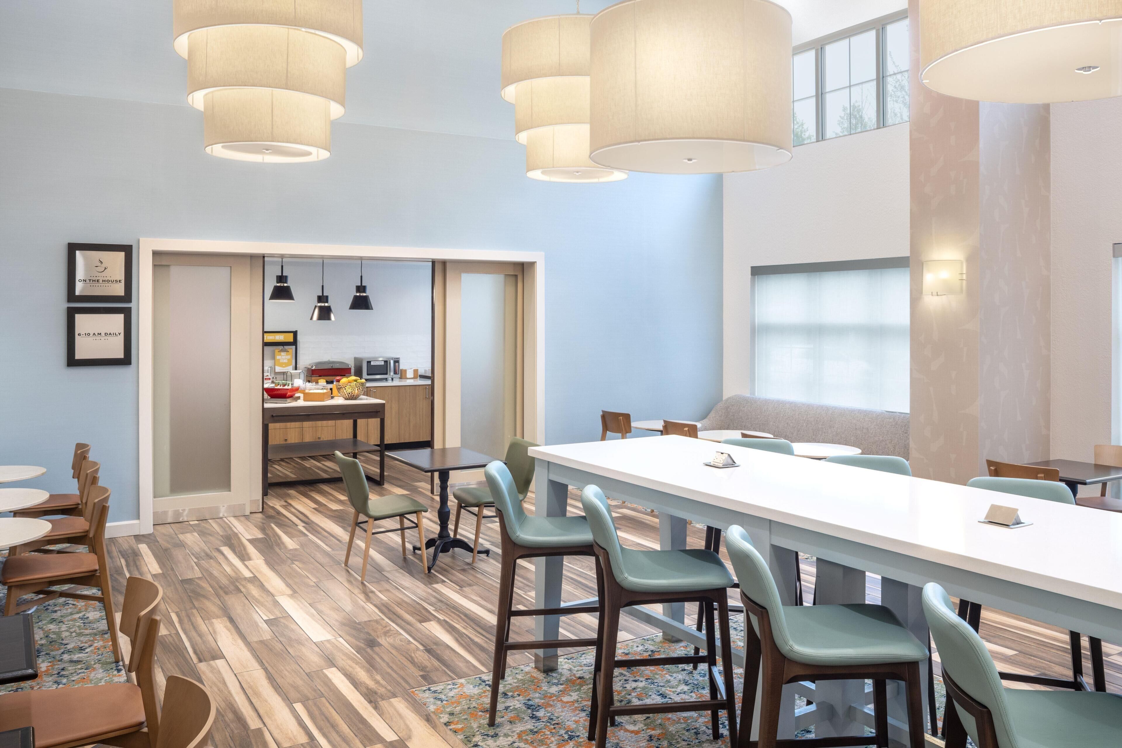 A modern dining area with a long table, chairs, and pendant lighting.