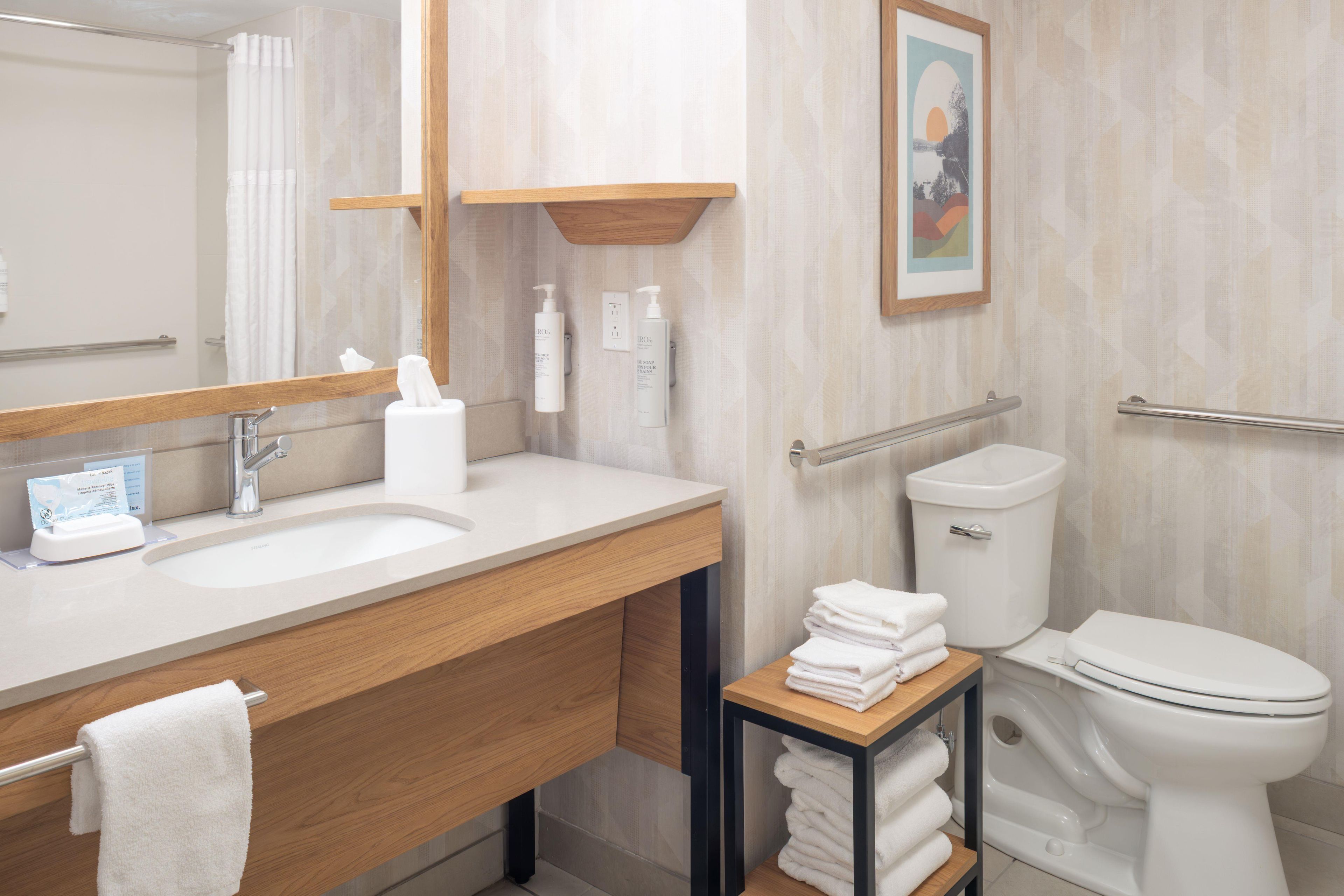 A modern bathroom with a wooden vanity, a sink, a toilet, and a small shelf with towels.