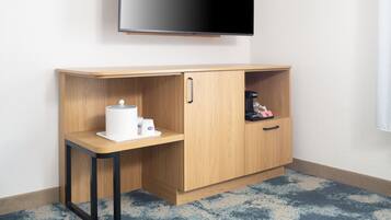 Una habitación de esquina con un escritorio de madera, un televisor montado en la pared y un mueble con una cafetera.