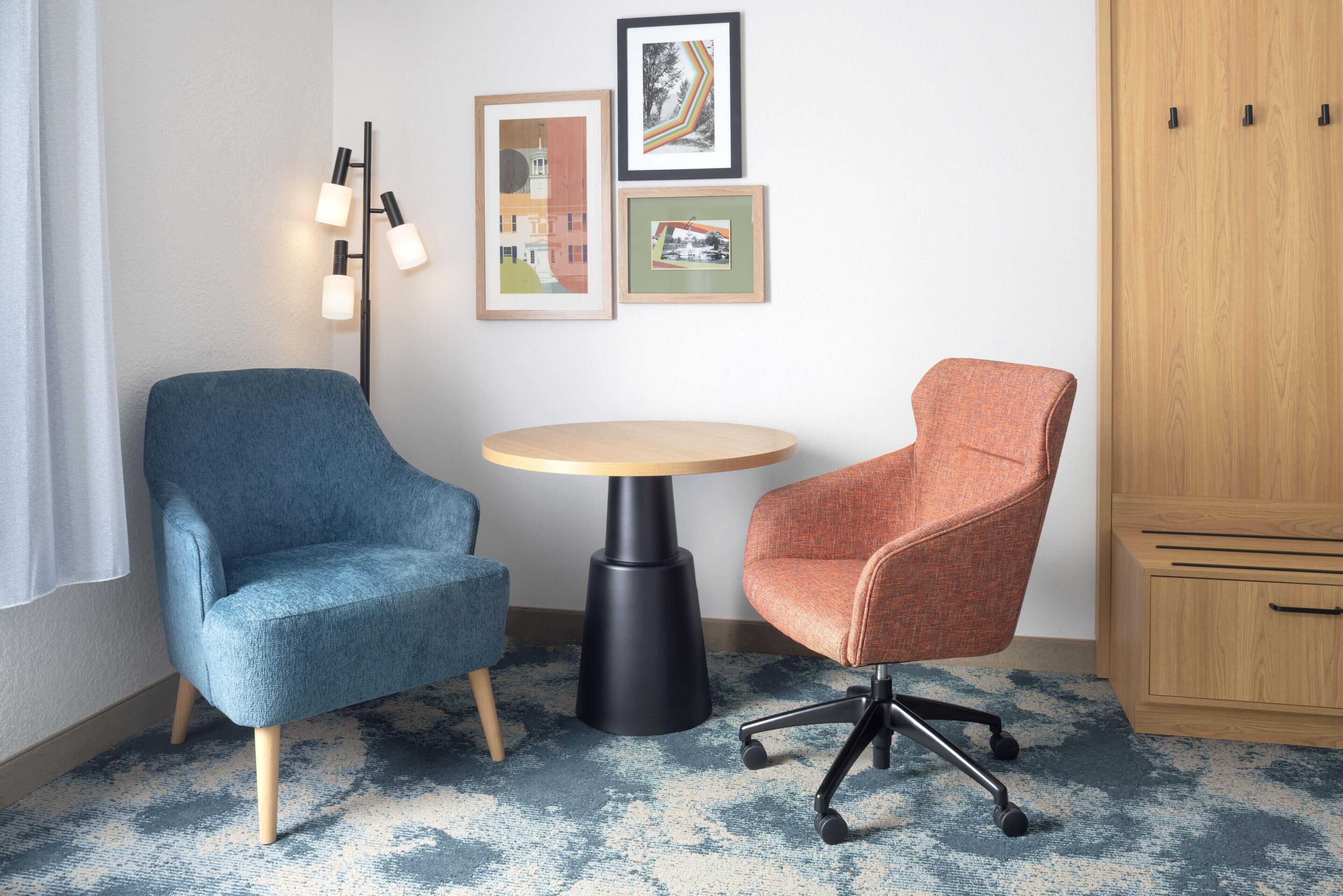 Una habitación con un sillón azul, un sillón naranja, una mesa redonda, una lámpara de pie y un armario.