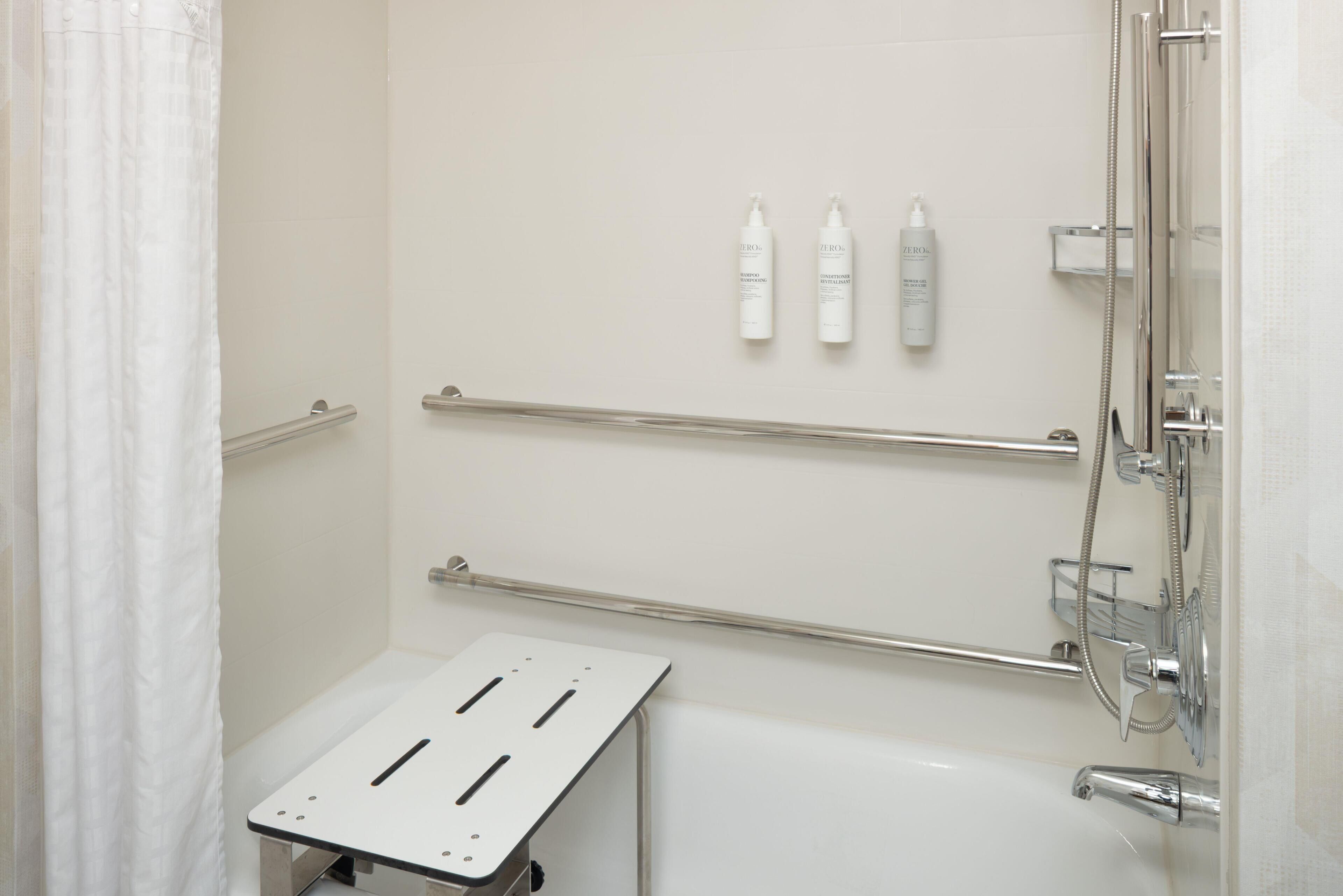 A shower area with a grab bar, a handheld showerhead, and three bottles of shampoo.