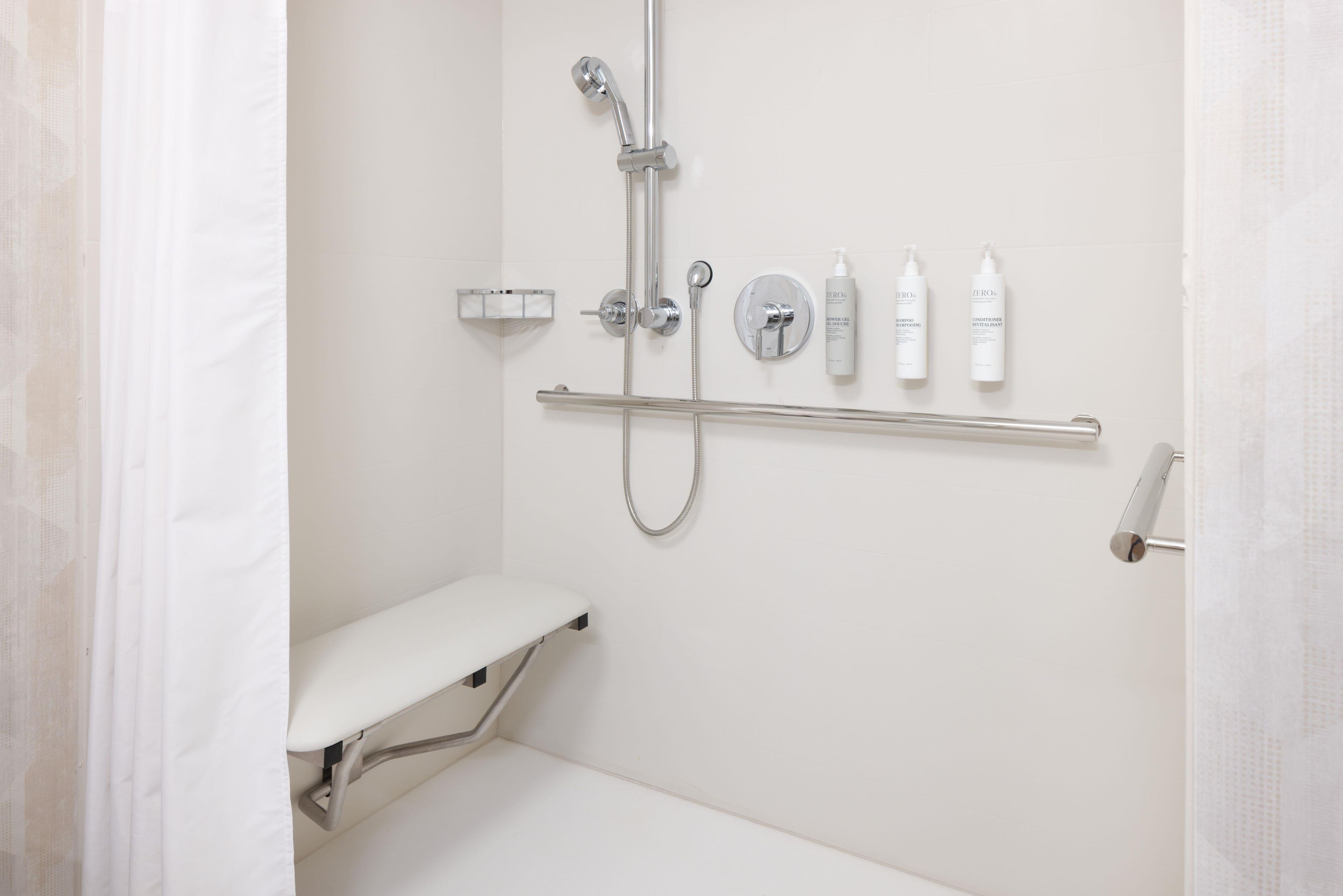 A modern bathroom with a shower, toilet, and handrails.