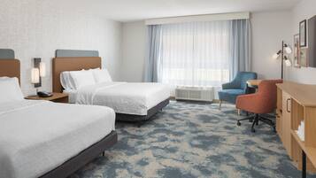 A hotel room with two beds, a desk, a chair, and a large window with curtains.