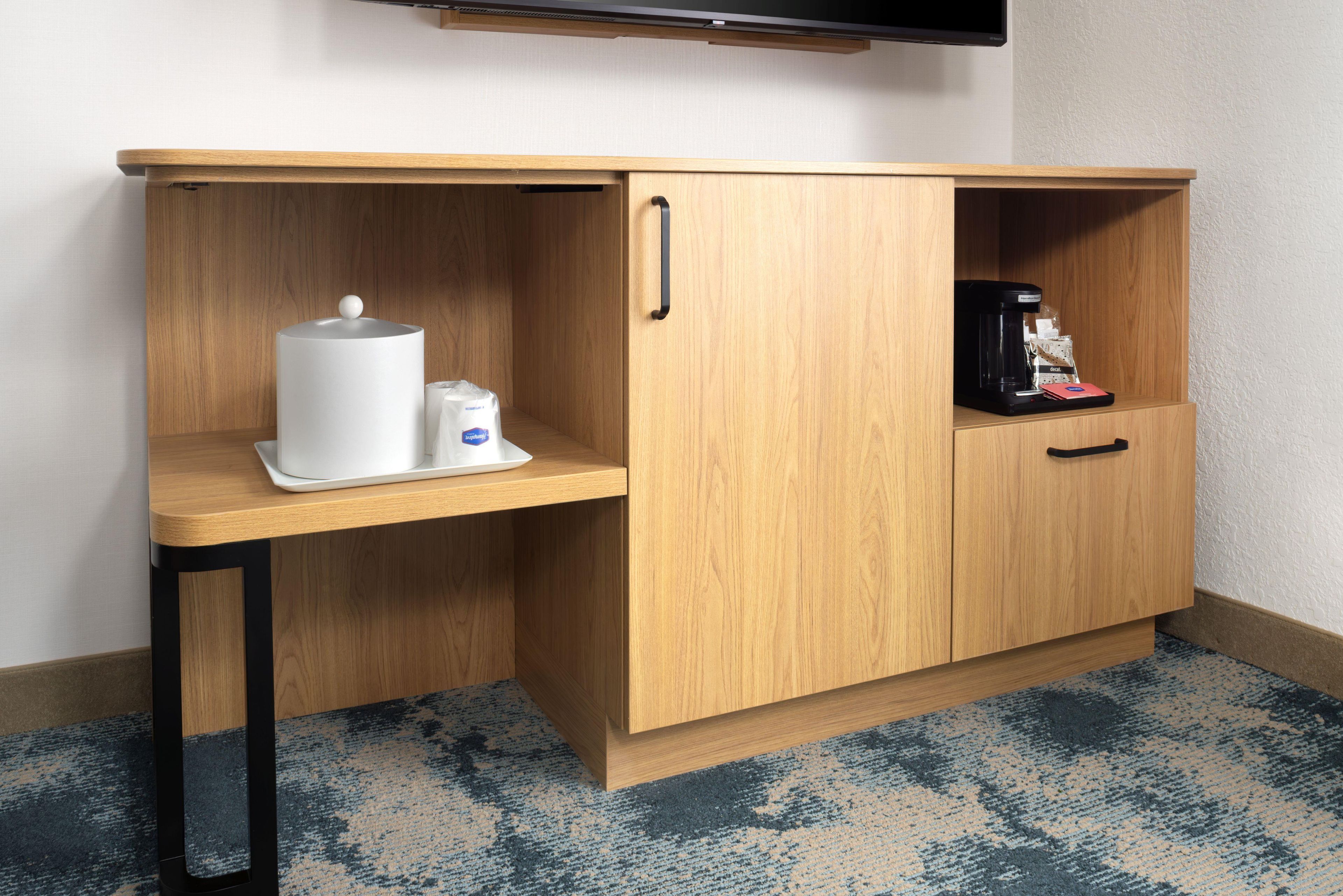 A wooden cabinet with a coffee maker and a white container.