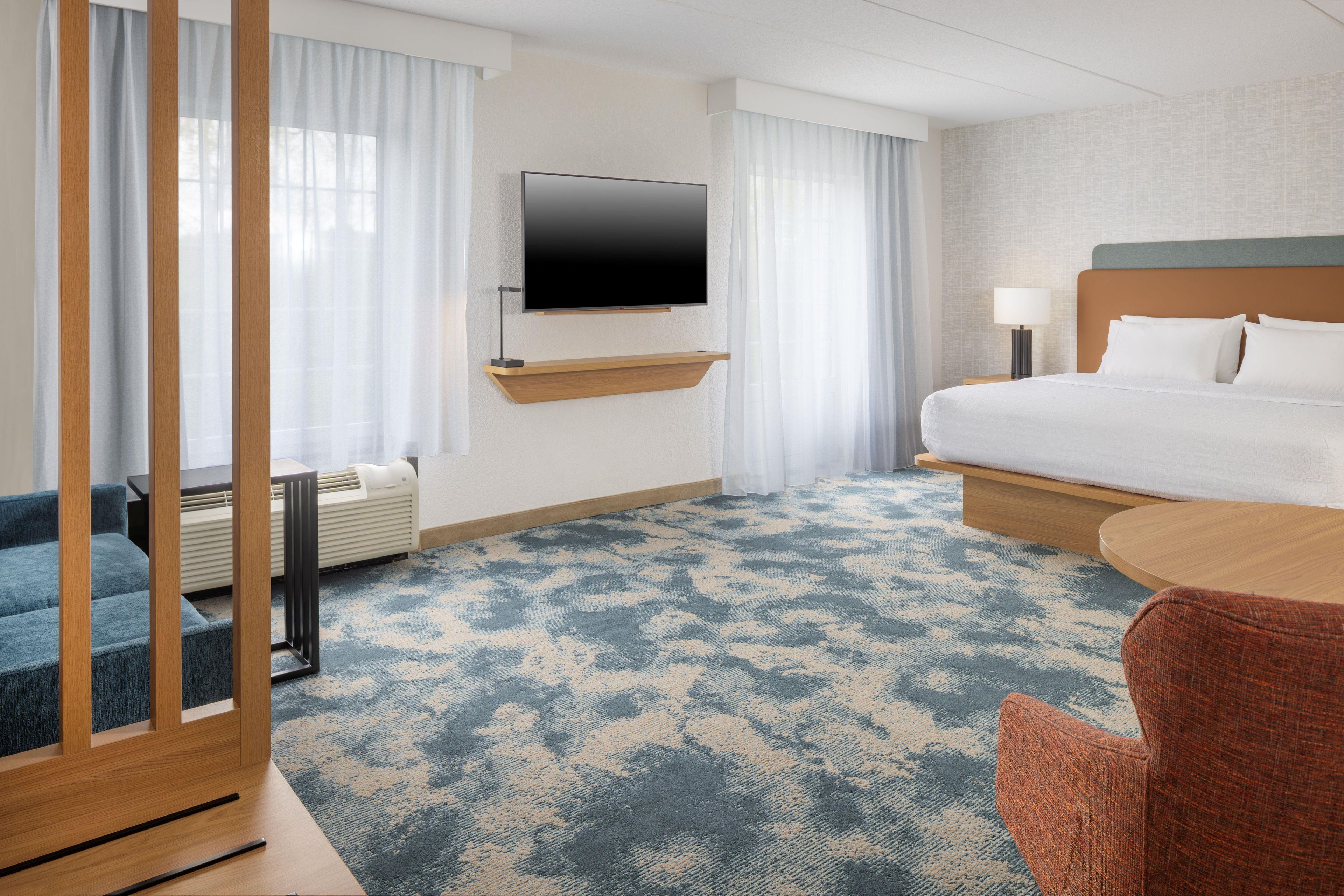 Habitación de hotel con cama, televisor montado en la pared, escritorio con silla y ventana con cortinas.