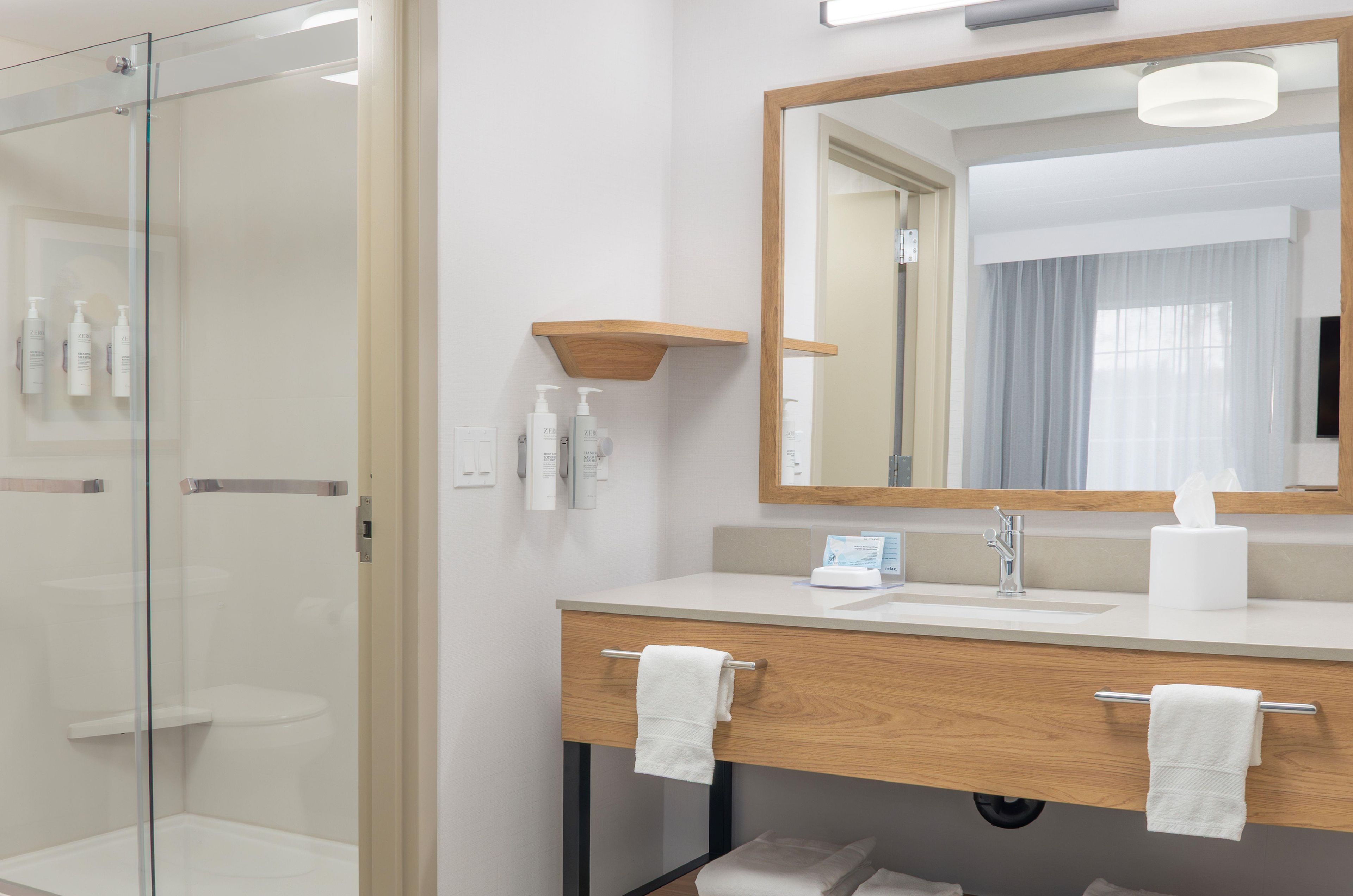 Un baño moderno con cabina de ducha de vidrio, tocador de madera con espejo y perchero.