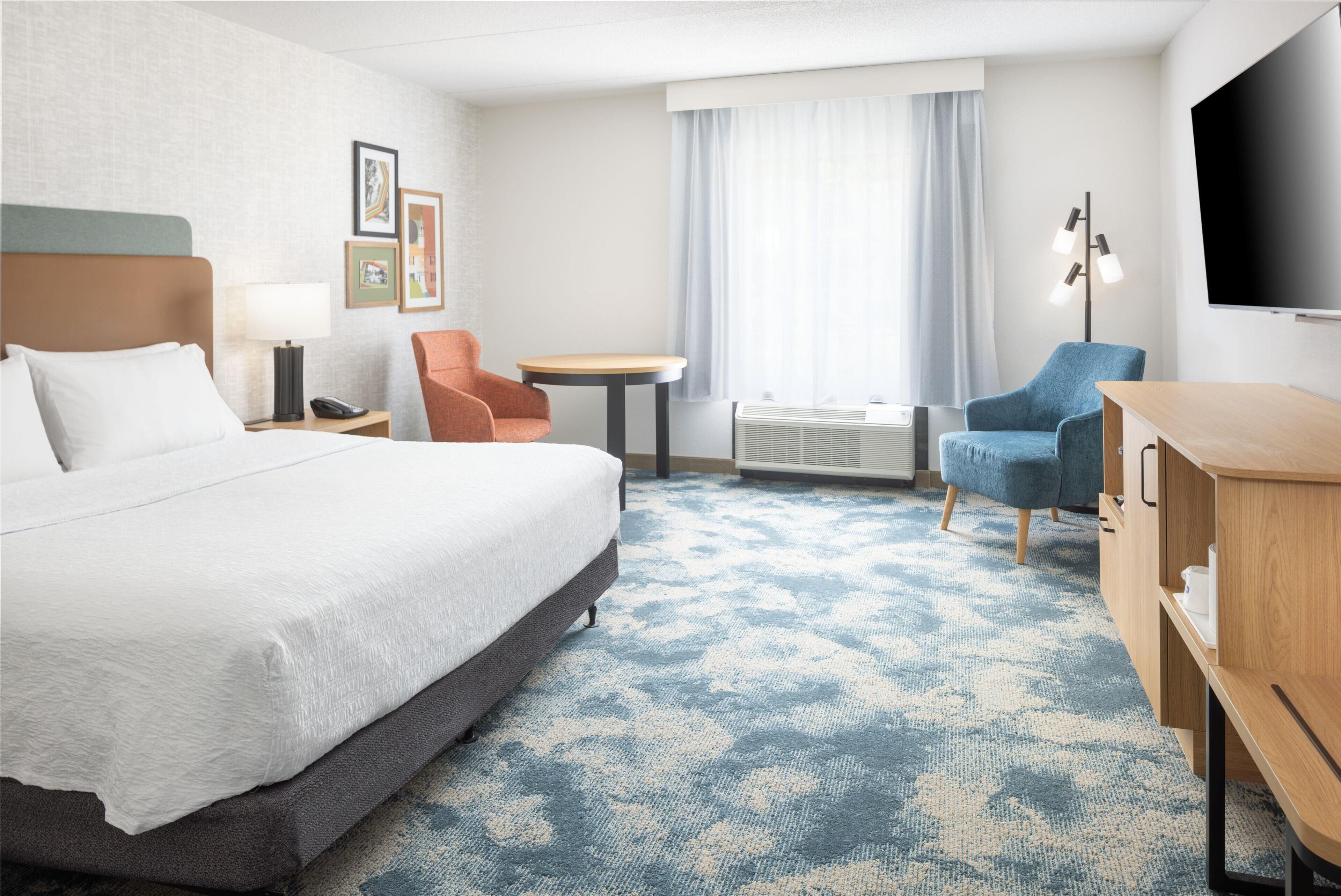 Ein Hotelzimmer mit einem Bett, einem Schreibtisch, einem Stuhl, einem Fernseher und einem Fenster mit Vorhängen.
