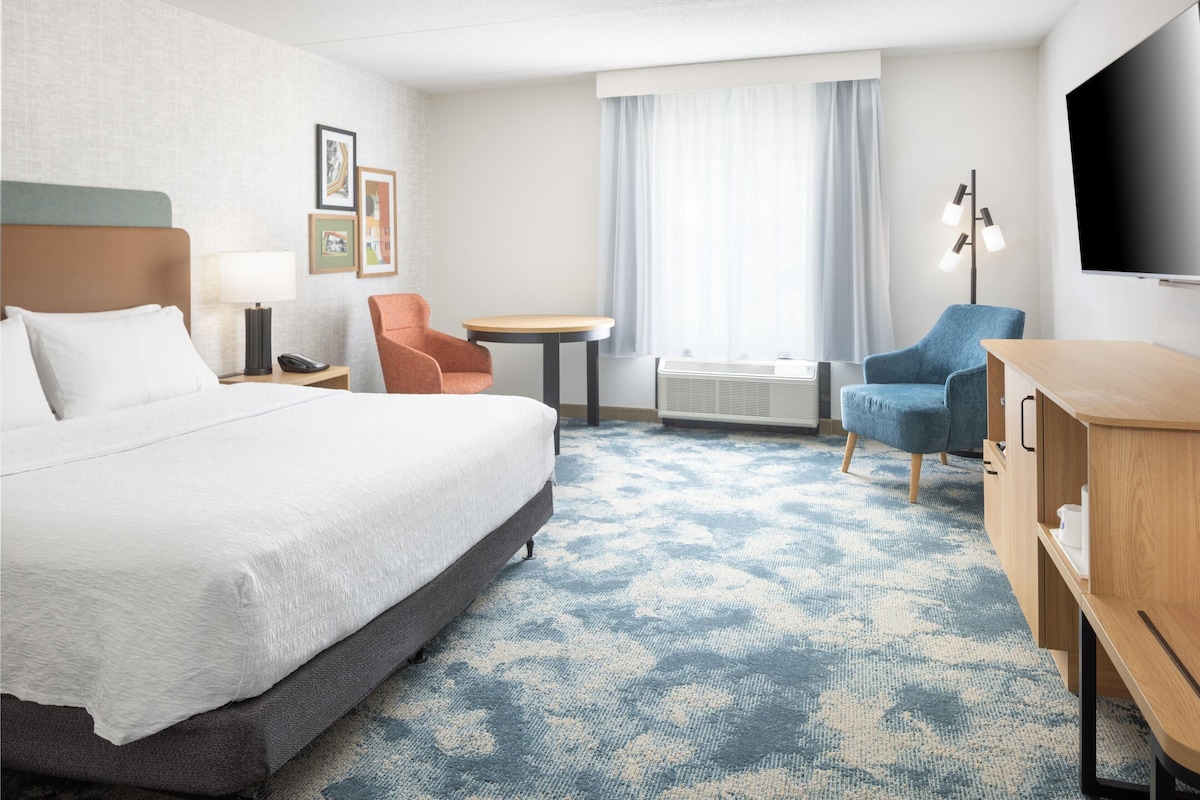 Une chambre d’hôtel avec un lit, un bureau, une chaise, une télévision et une fenêtre avec des rideaux.