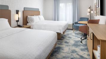 A hotel room with two beds, a desk, a chair, a lamp, and a large window with curtains.