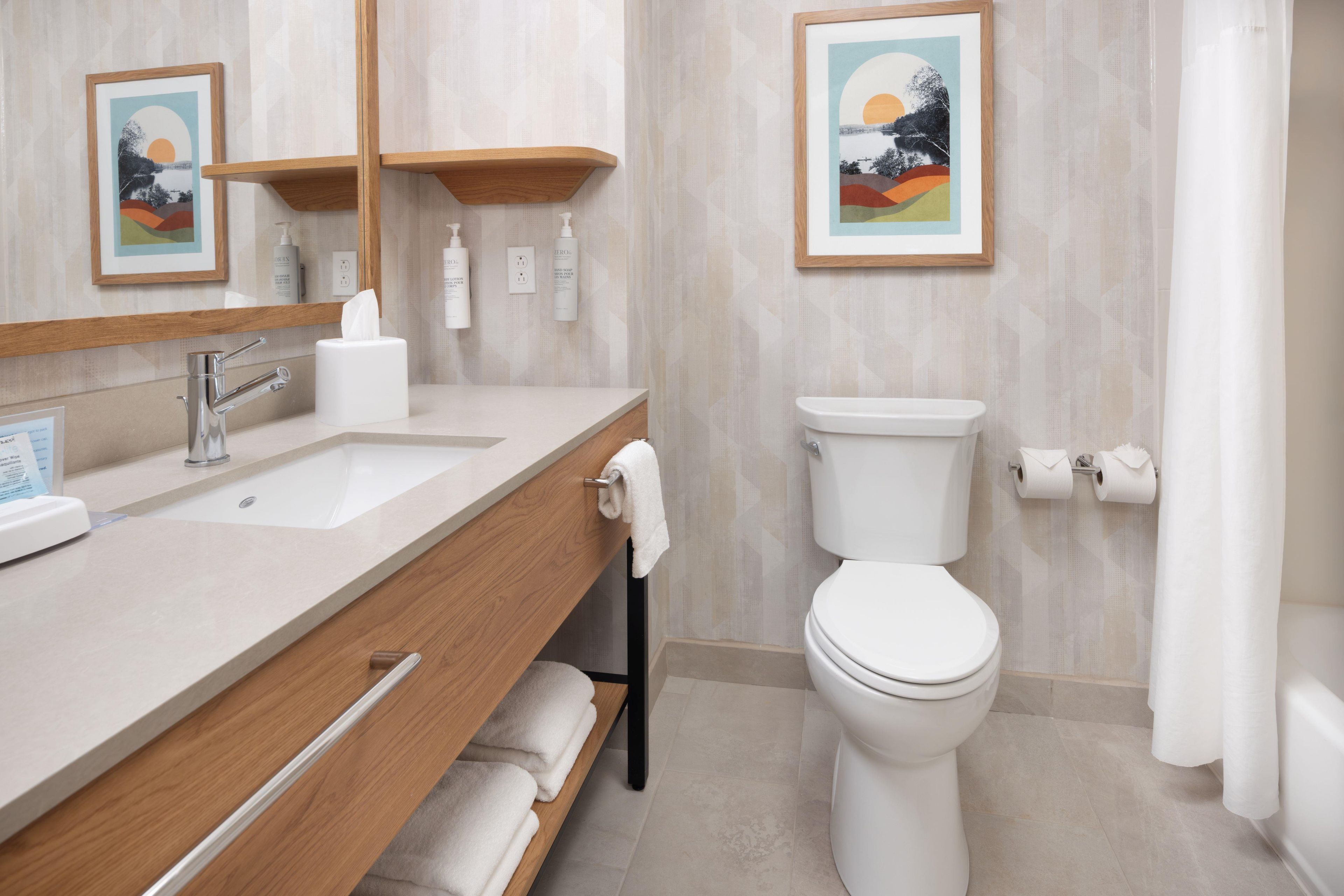 A modern bathroom with a wooden vanity, a toilet, and two framed pictures on the wall.