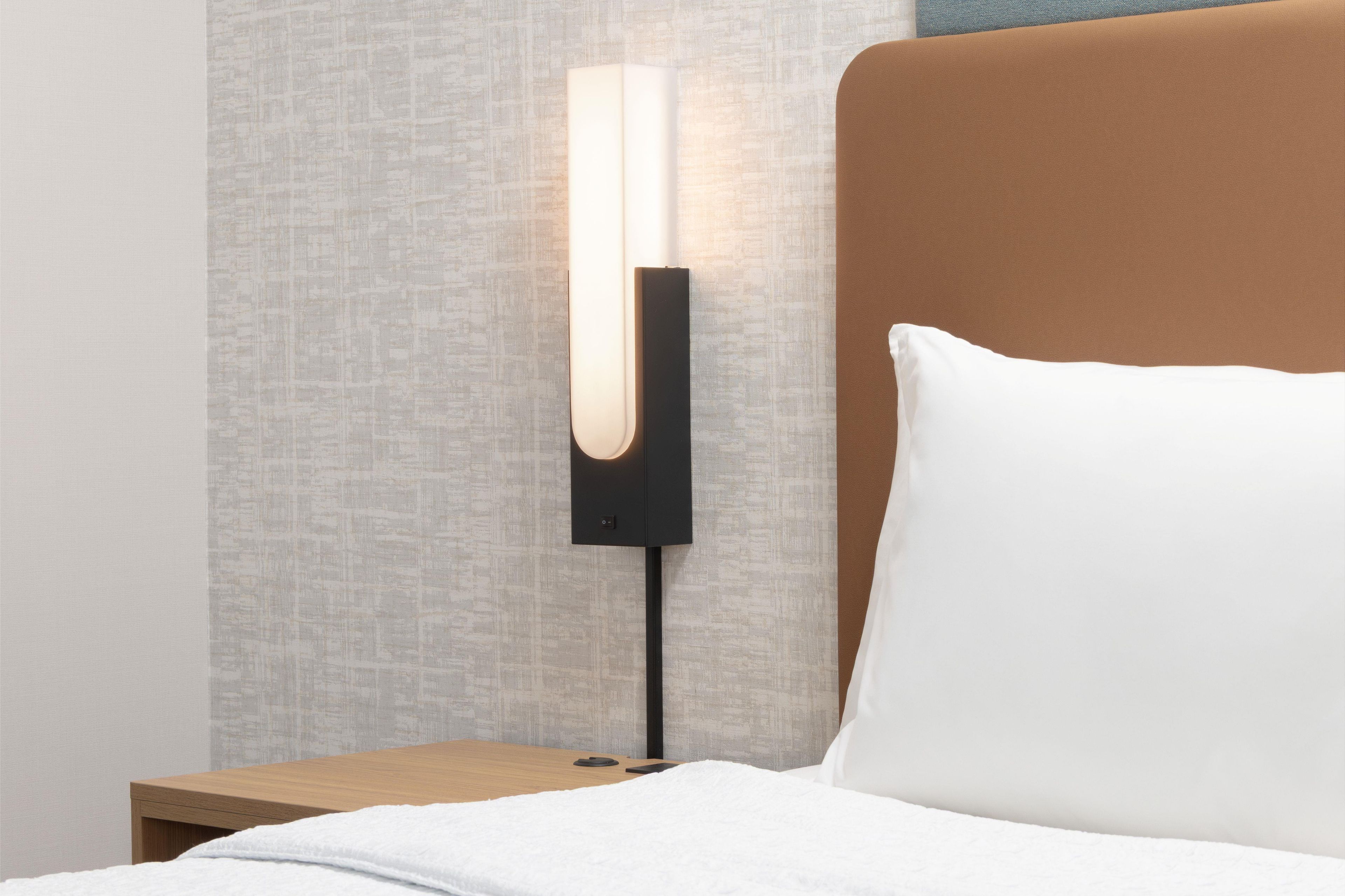 Ein Bett mit einem weißen Kopfkissen und einem Nachttisch mit einer modernen Lampe.