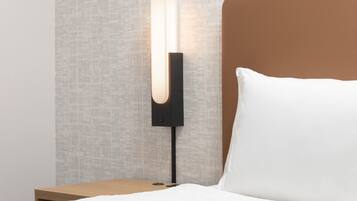 Ein Bett mit einem weißen Kopfkissen und einem Nachttisch mit einer modernen Lampe.
