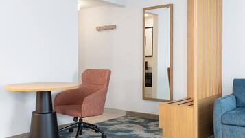 A room with a round table, an office chair, a mirror, and a blue sofa.