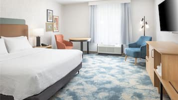 Habitación de hotel con cama, escritorio, silla, televisor y ventana con cortinas.