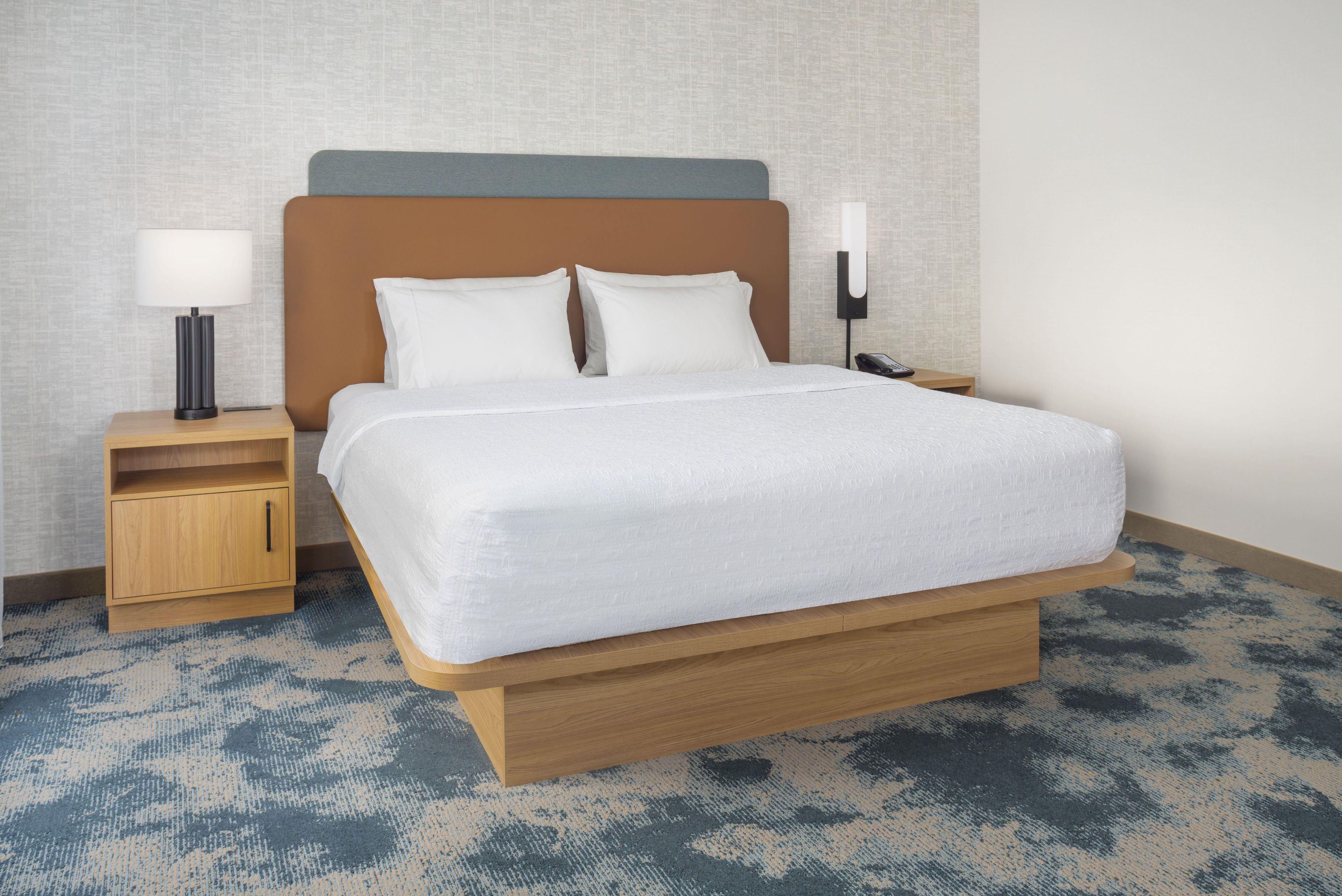 Una habitación de hotel con una cama grande, mesitas de noche de madera, una lámpara y un teléfono.