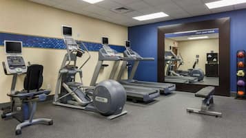 A gym with treadmills, elliptical machines, and a mirrored wall.