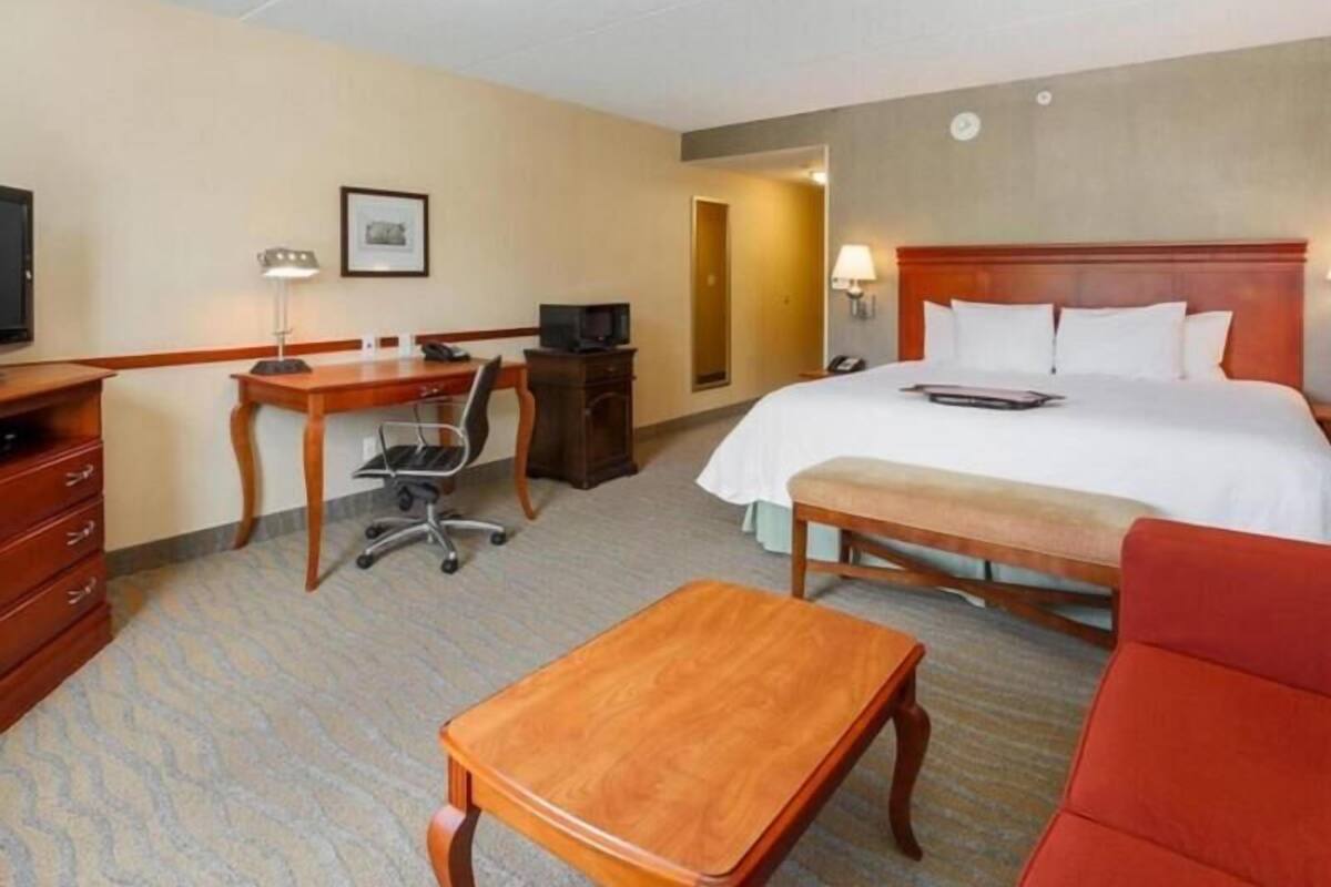 A hotel room with a bed, desk, chair, television, and a small table.
