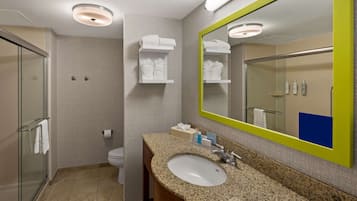 Un bany modern amb un lavabo amb taulell de granat, un gran mirall amb marc verd i una dutxa amb envàs de vidre.