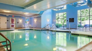 An indoor swimming pool with clear water, a lifeguard chair, and a sunlit area with lounge chairs.