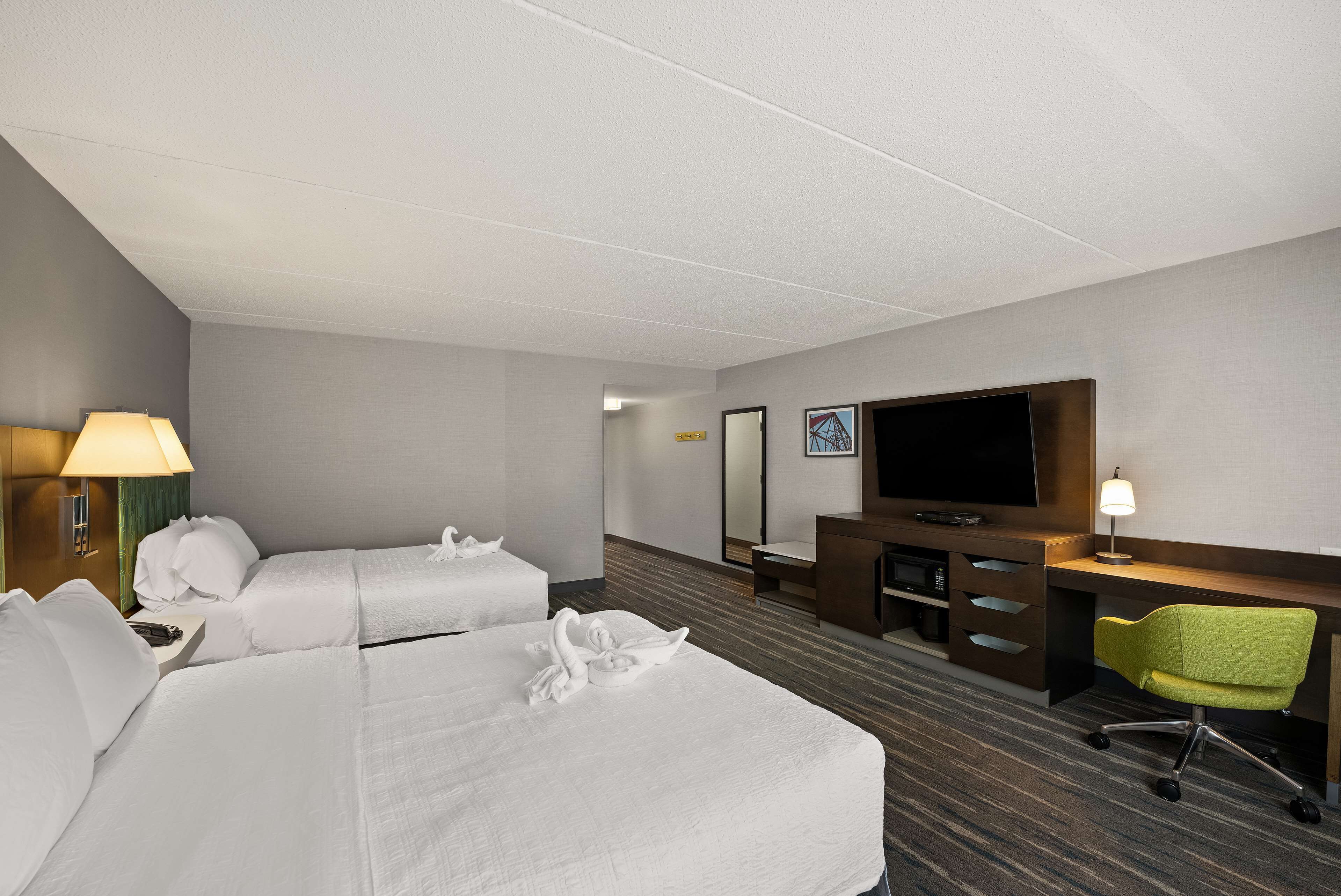 A hotel room with two beds, a TV, a desk with a chair, and a lamp.