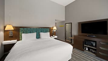 A hotel room with a large bed, two bedside tables with lamps, a TV, a mirror, and a minibar.