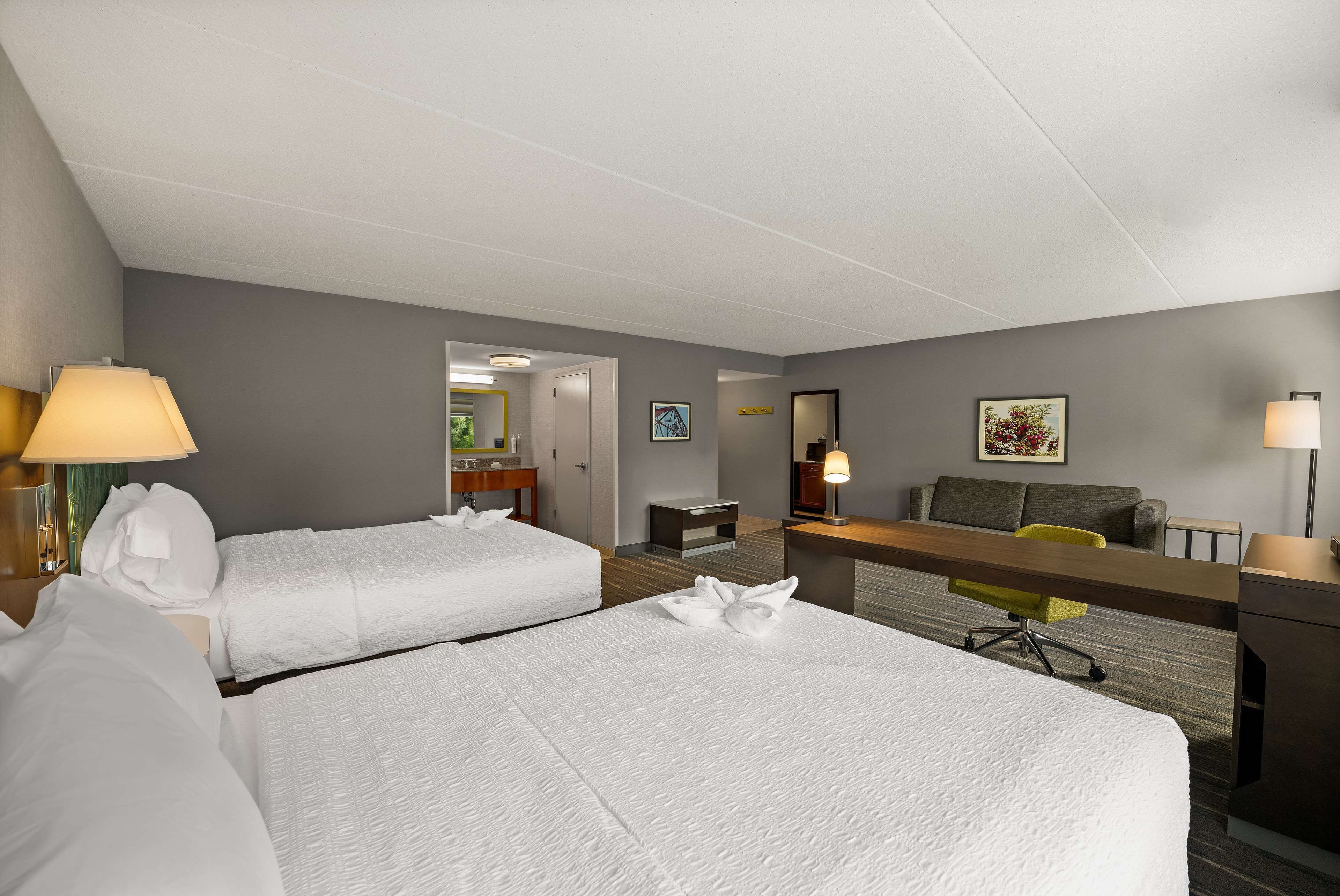 A hotel room with two beds, a desk, a chair, and a sofa.