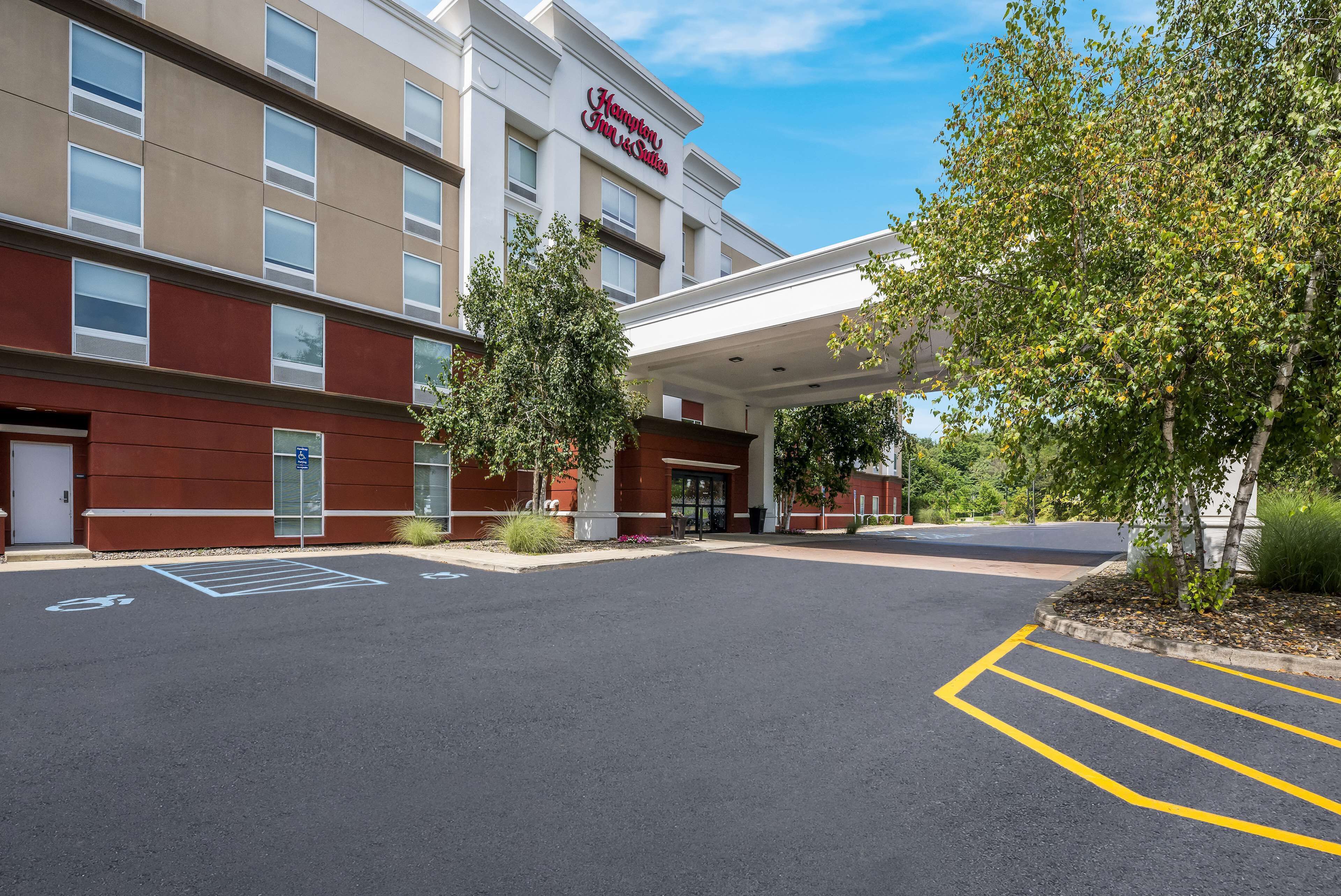 Un Hampton Inn & Suites con estacionamiento, entrada cubierta y fachada de color rojo y beige.