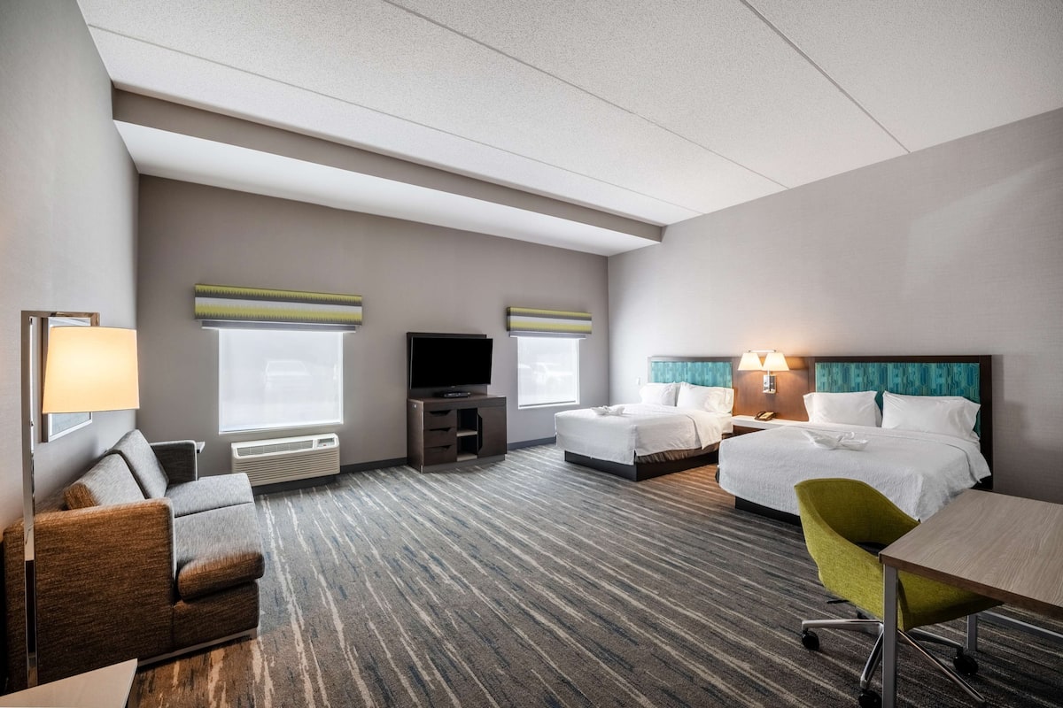 A hotel room with a sofa, two beds, a TV, a desk, and a chair.