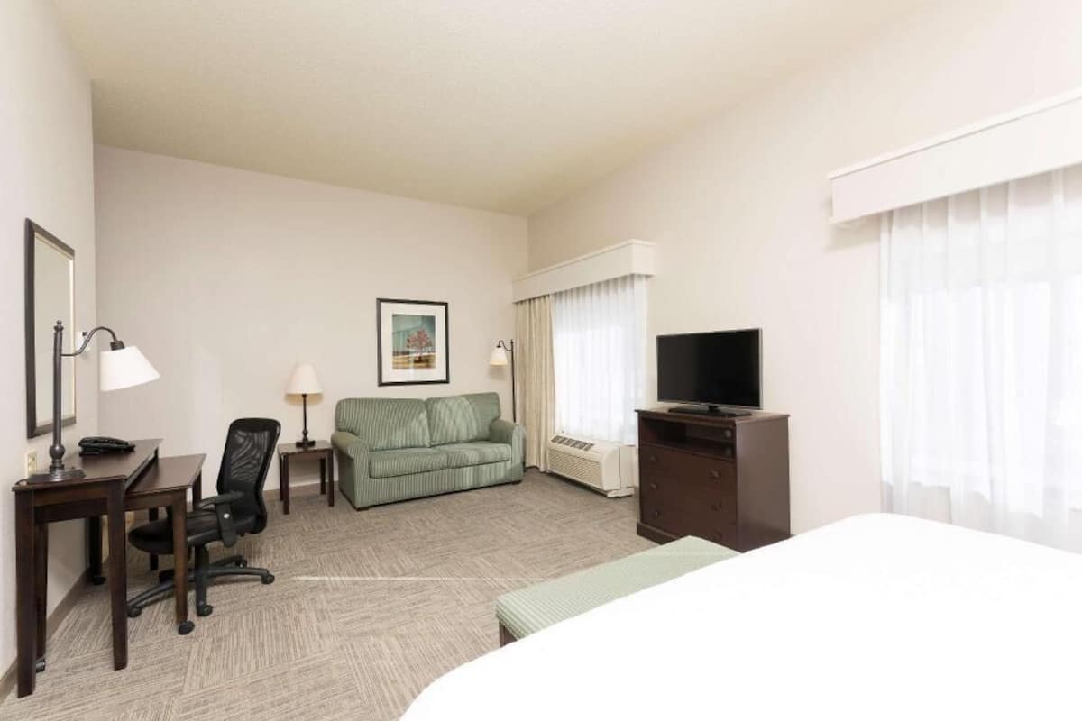 A hotel room with a bed, a desk with a chair, a sofa, a television, and a picture on the wall.