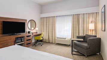 Een hotelkamer met een bed, een bureau met een flatscreen televisie, een stoel, een lamp en een raam met gordijnen.
