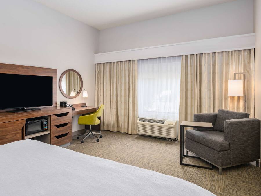 Een hotelkamer met een bed, een bureau met een flatscreen televisie, een stoel, een lamp en een raam met gordijnen.
