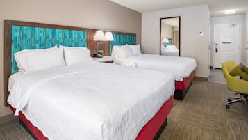 A hotel room with two beds, a desk, a chair, and a mirror.
