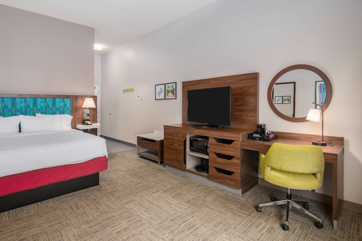 A hotel room with a bed, a desk with a computer, a chair, a TV, and a mirror.