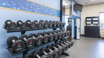 A gym with multiple rows of dumbbells on racks, a television mounted on the wall, and a water cooler.