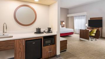 A hotel room with a kitchenette, a bed, a TV, and a desk.