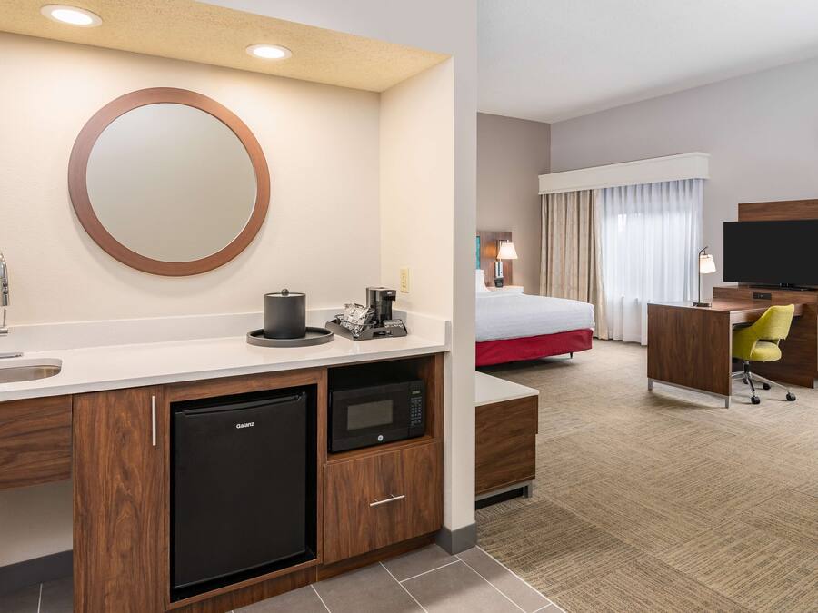 Quarto de hotel com cozinha compacta, cama, televisão e escrivaninha.