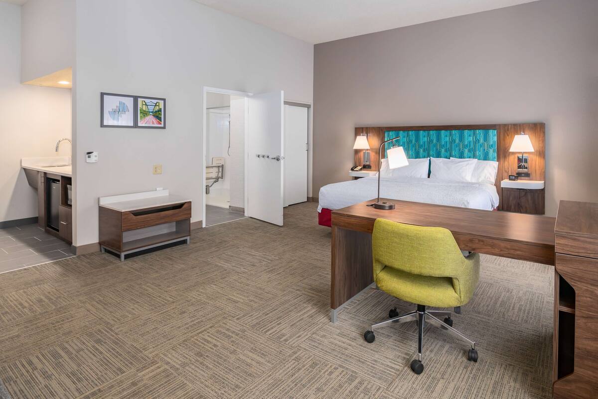 A hotel room with a bed, desk, chair, and a bathroom with a sink and mirror.
