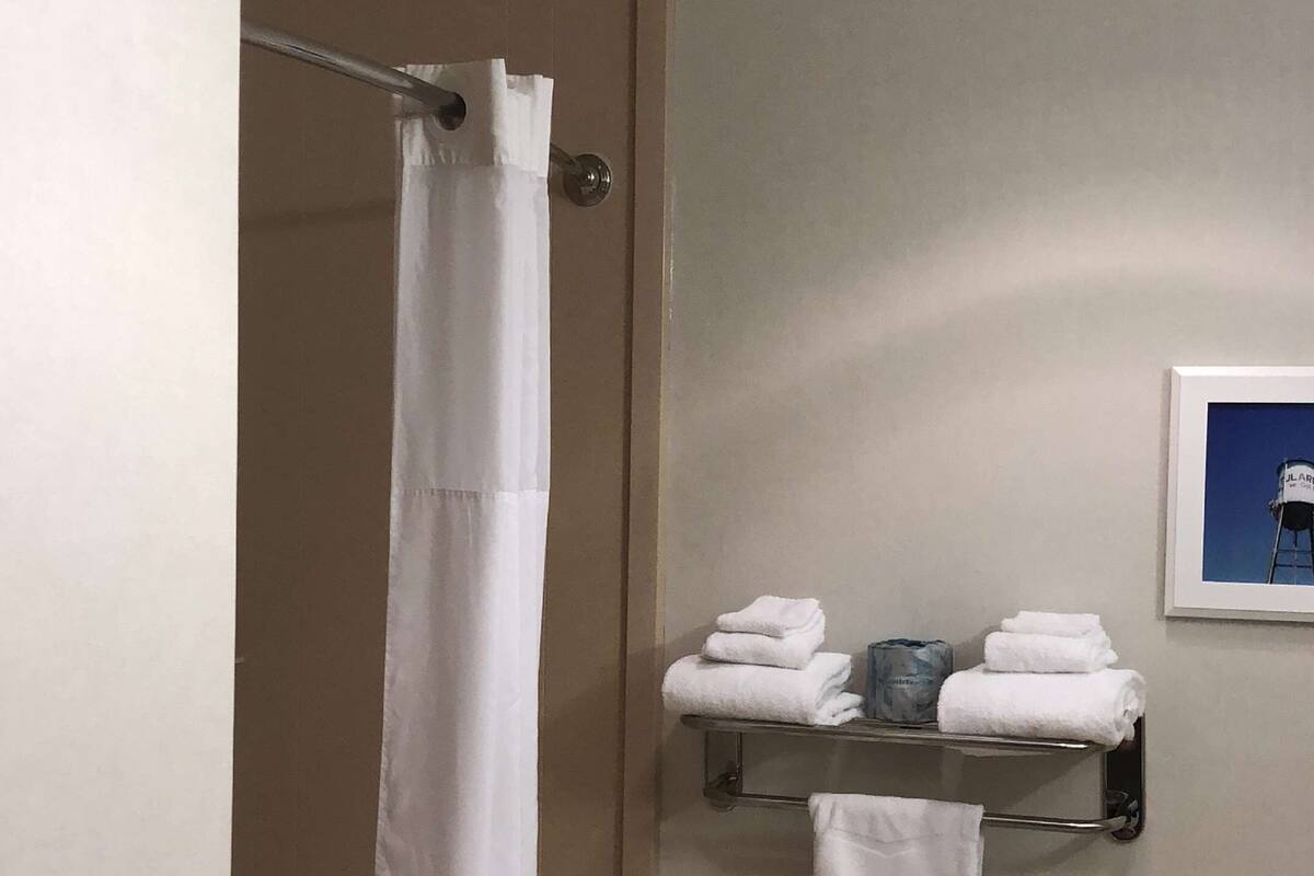A bathroom with a shower curtain, a towel rack with folded towels, a handrail, and a framed picture on the wall.