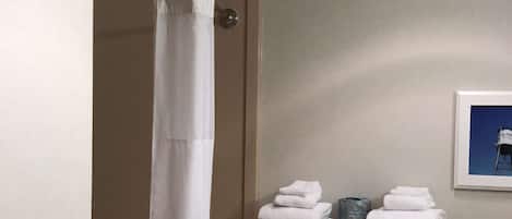 Um banheiro com cortina de chuveiro, porta-toalhas com toalhas dobradas, corrimão e um quadro na parede.