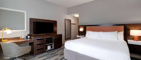 A hotel room with a large bed, a desk with a flat-screen TV, a chair, and a desk lamp.