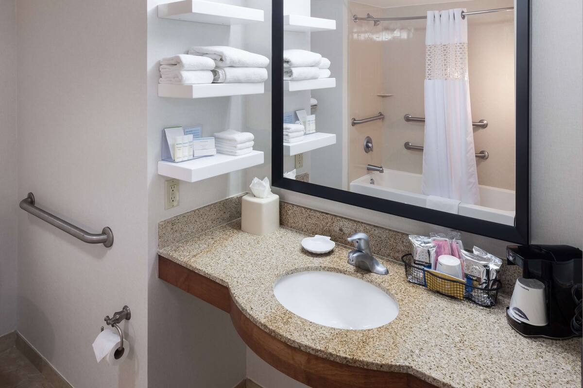 A bathroom with a sink, mirror, towel racks, and a shower area.