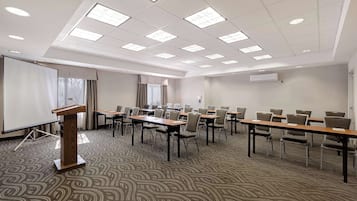 Uma sala de conferências com palestrino, mesas, cadeiras e tela de projeção.