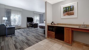 Habitación de hotel con sofá, escritorio, televisión, cama y kitchenette, además de un cuadro en la pared.