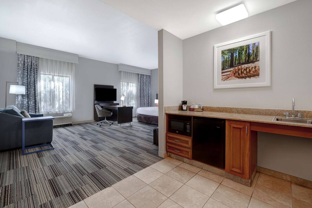 A hotel room with a sofa, a desk, a television, a bed, a kitchenette, and a framed picture on the wall.