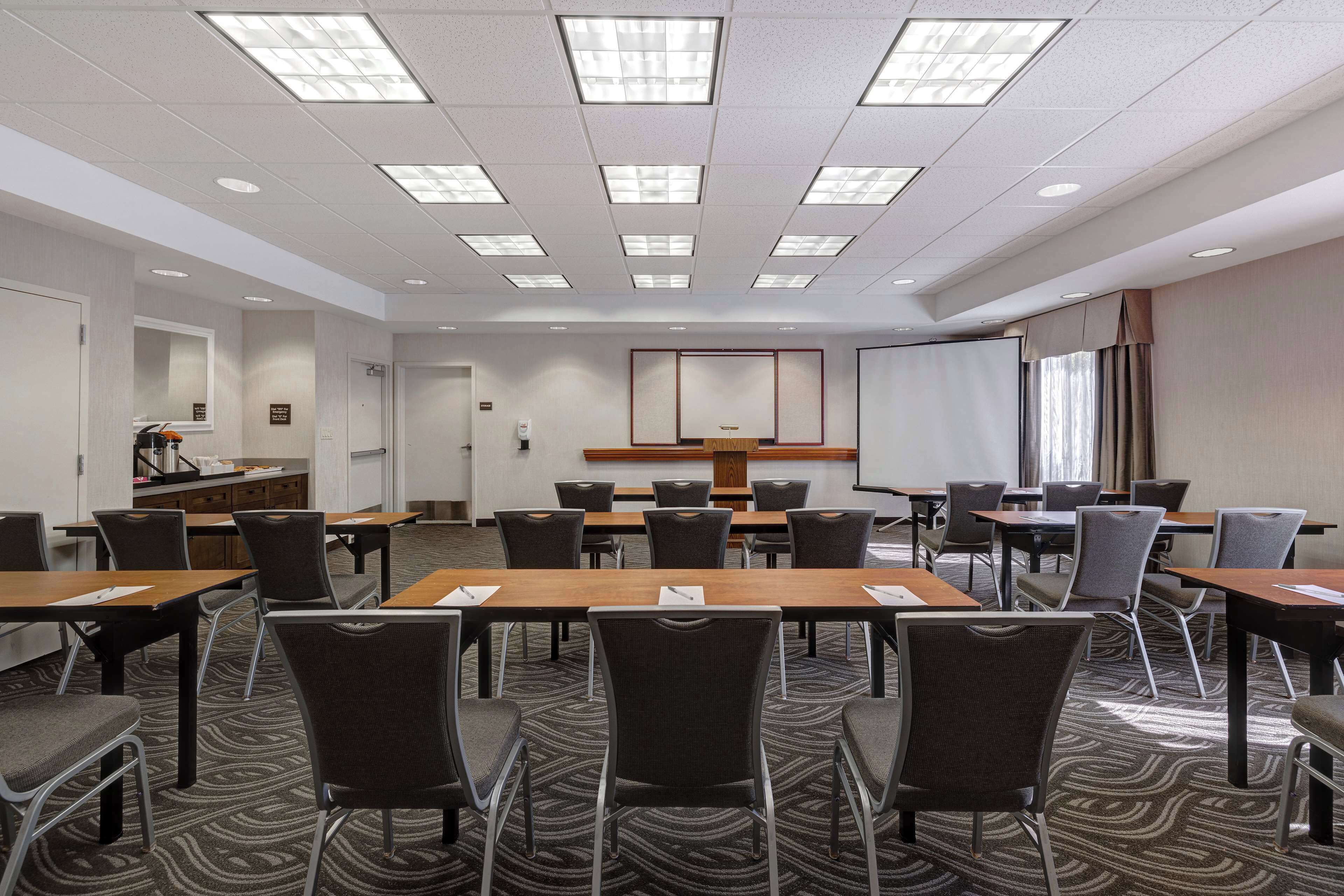 A conference room with a long table, multiple chairs, a projector screen, and a podium.