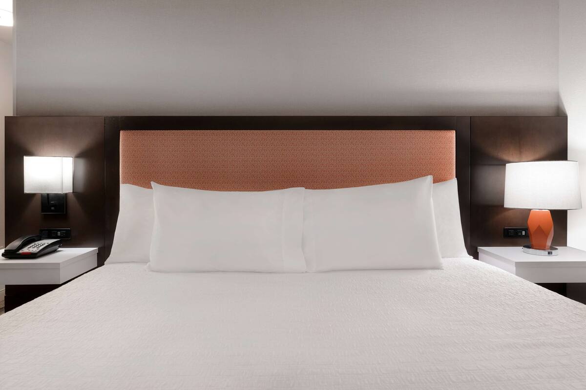 A hotel room with a large bed, two bedside tables, a telephone, and two lamps.