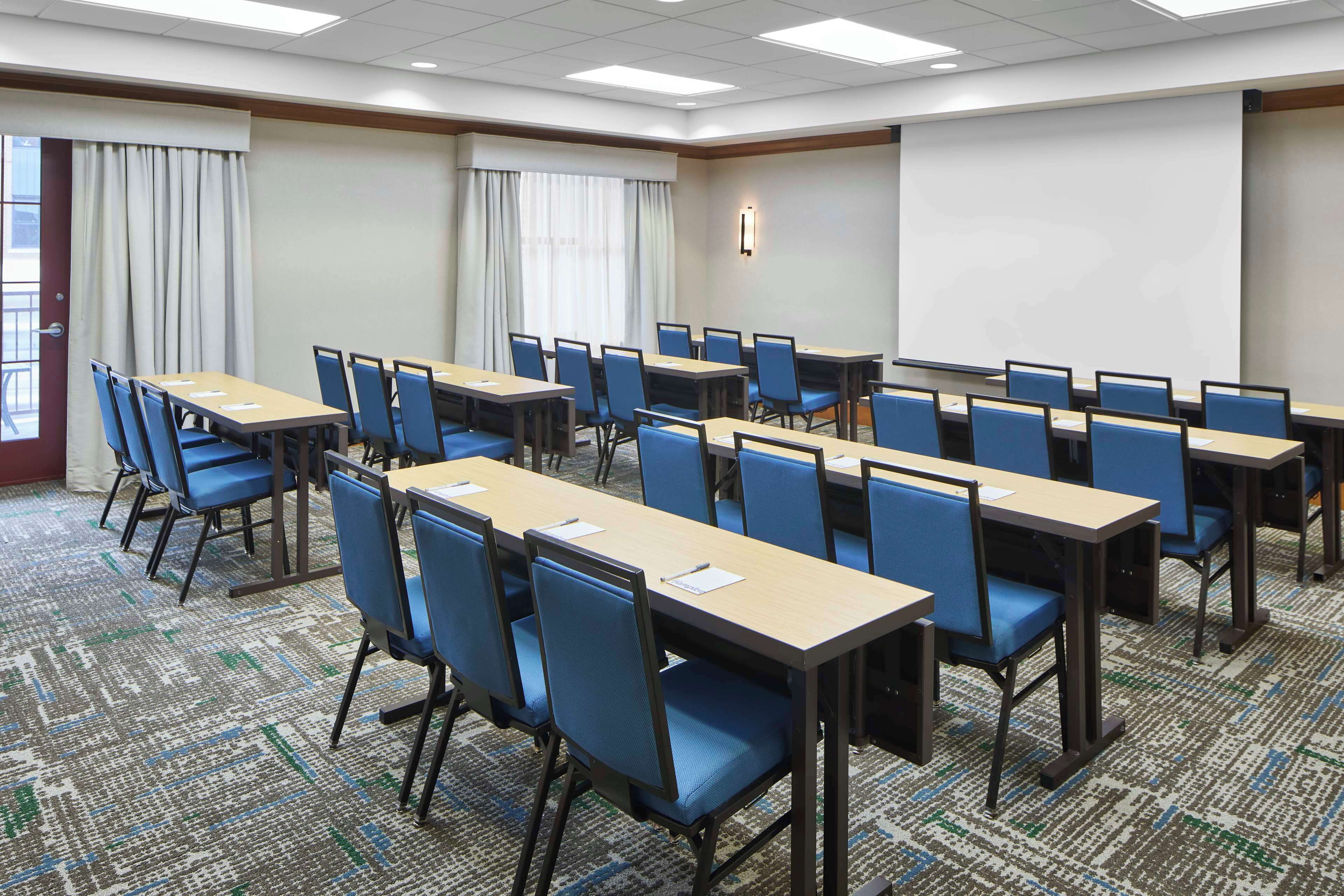 A conference room with multiple tables and chairs, a projector screen, and a carpeted floor.